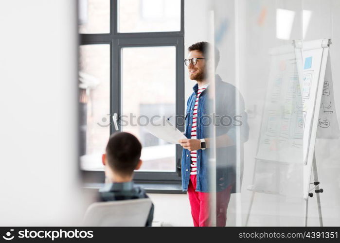 business, technology and people concept - creative man with user interface design on flip chart at office presentation. creative man with papers at office presentation. creative man with papers at office presentation