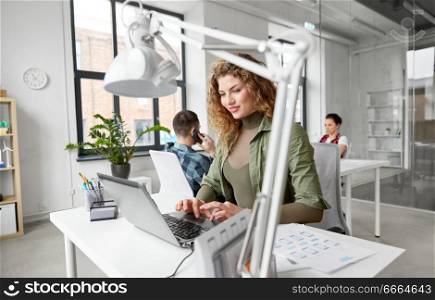 business, technology and people concept - creative woman with laptop computer working on user interface design at office. creative woman with laptop working at office