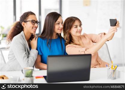 business, technology and people concept - female team or businesswomen taking selfie at office. happy businesswomen taking selfie at office. happy businesswomen taking selfie at office