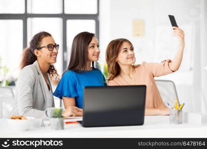 business, technology and people concept - female team or businesswomen taking selfie at office. happy businesswomen taking selfie at office. happy businesswomen taking selfie at office