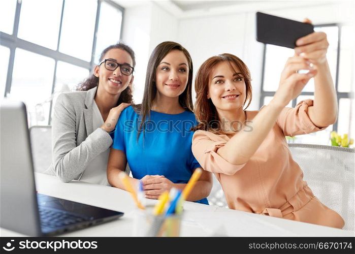 business, technology and people concept - female team or businesswomen taking selfie at office. happy businesswomen taking selfie at office. happy businesswomen taking selfie at office