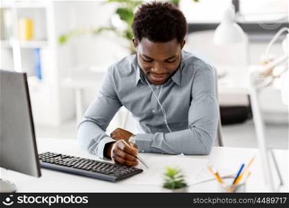 business, technology and people concept - happy african american businessman with earphones and papers listening to music at office. businessman with earphones and papers at office. businessman with earphones and papers at office