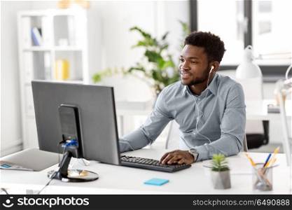 business, technology and people concept - happy african american businessman with earphones and computer computer listening to music at office. businessman with earphones and computer at office. businessman with earphones and computer at office