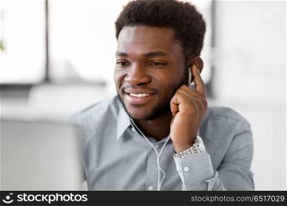business, technology and people concept - happy african american businessman with earphones and computer listening to music at office. businessman with earphones and computer at office. businessman with earphones and computer at office