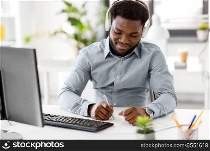 business, technology and people concept - happy african american businessman with headphones and papers listening to music at office. businessman with headphones and papers at office. businessman with headphones and papers at office