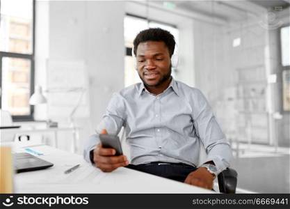business, technology and people concept - happy african american businessman with headphones and smartphone listening to music at office. businessman with headphones and smartphone. businessman with headphones and smartphone