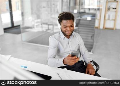 business, technology and people concept - happy african american businessman with headphones and smartphone listening to music at office. businessman with headphones and smartphone. businessman with headphones and smartphone