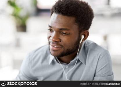business, technology and people concept - happy african american man with earphones listening to music at office. man with earphones listening to music at office. man with earphones listening to music at office