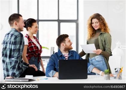 business, technology and people concept - happy creative team with laptop computer and papers working at office. creative team with laptop working at office. creative team with laptop working at office