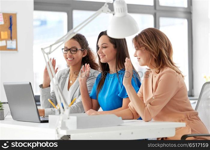 business, technology and people concept - happy smiling businesswomen having video chat by laptop computer at office. businesswomen having video chat at office. businesswomen having video chat at office