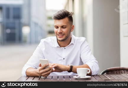 business, technology and people concept - happy young man with smartphone and coffee cup texting at city street cafe