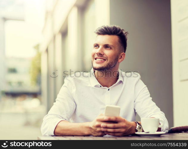 business, technology and people concept - happy young man with smartphone and coffee cup texting at city street cafe. man with smartphone and coffee at city cafe