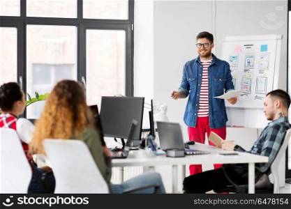 business, technology and people concept - man showing user interface design on flip chart to creative team at office presentation. creative man showing user interface at office. creative man showing user interface at office