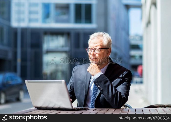 business, technology and people concept - senior businessman with laptop computer at city street cafe