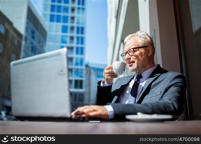business, technology and people concept - senior businessman with laptop computer drinking coffee at city street cafe