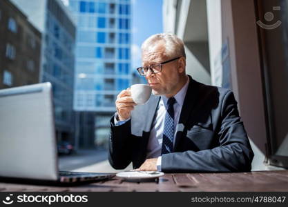 business, technology and people concept - senior businessman with laptop computer drinking coffee at city street cafe