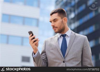 business, technology and people concept - serious businessman with smartphone over office building