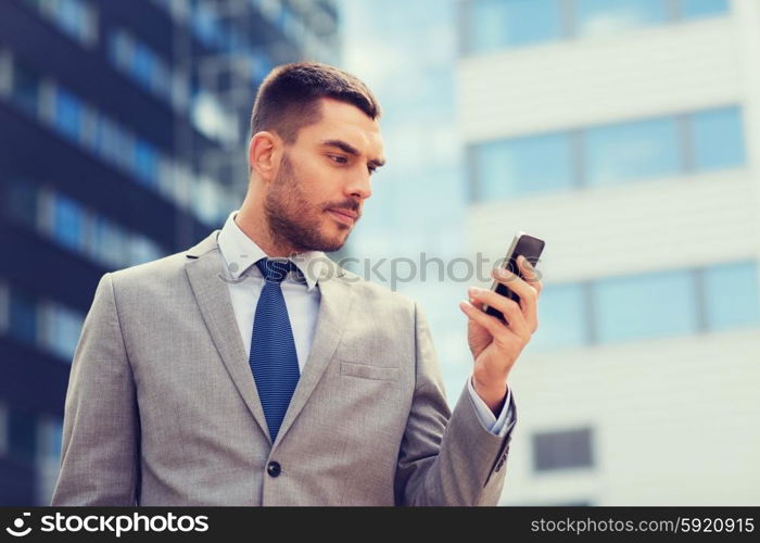 business, technology and people concept - serious businessman with smartphone over office building