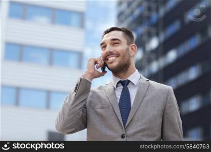 business, technology and people concept - smiling businessman with smartphone talking over office building