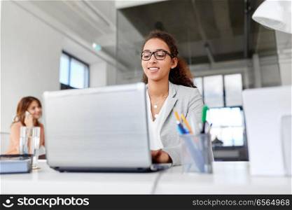 business, technology and people concept - smiling businesswoman in glasses with laptop computer working at office. happy businesswoman with laptop working at office