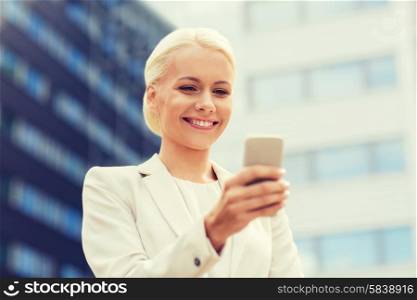 business, technology and people concept - smiling businesswoman with smartphone over office building