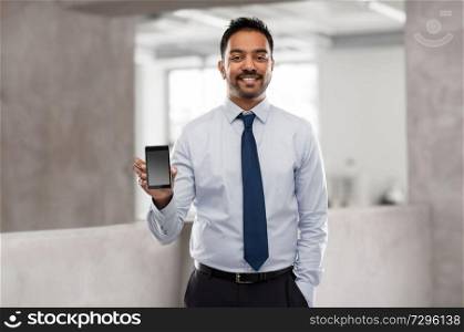 business, technology and people concept - smiling indian businessman with smartphone over office background. indian businessman with smartphone at office