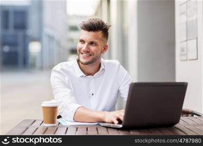 business, technology and people concept - smiling man with laptop computer and coffee cup at city street cafe