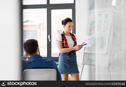 business, technology and people concept - woman showing tablet pc computer and user interface design on flip chart to creative team at office presentation. woman showing tablet pc to creative team at office. woman showing tablet pc to creative team at office