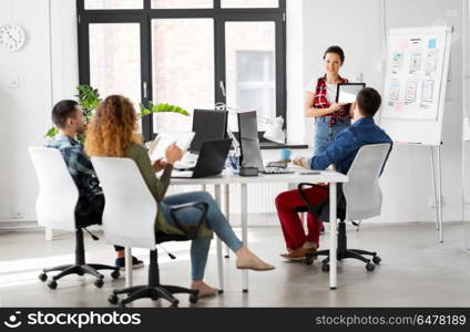 business, technology and people concept - woman showing tablet pc computer and user interface design on flip chart to creative team at office presentation. woman showing tablet pc to creative team at office. woman showing tablet pc to creative team at office