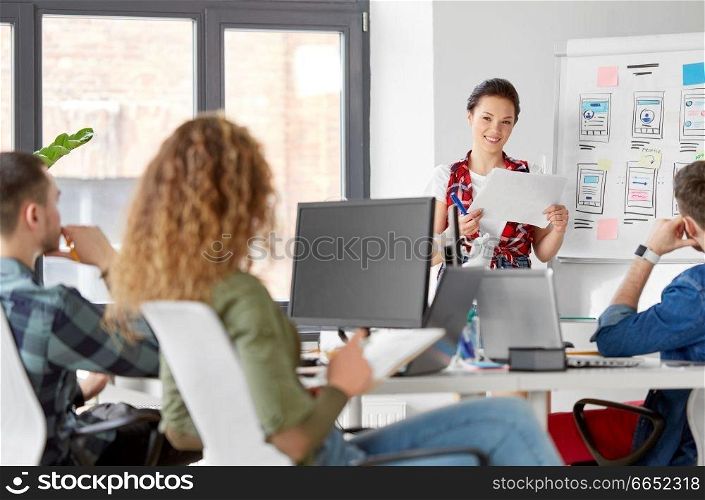 business, technology and people concept - woman showing user interface design on flip chart to creative team at office presentation. creative woman showing user interface at office