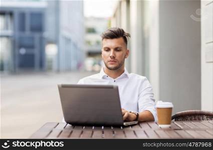 business, technology and people concept - young man with laptop computer and coffee cup at city street cafe