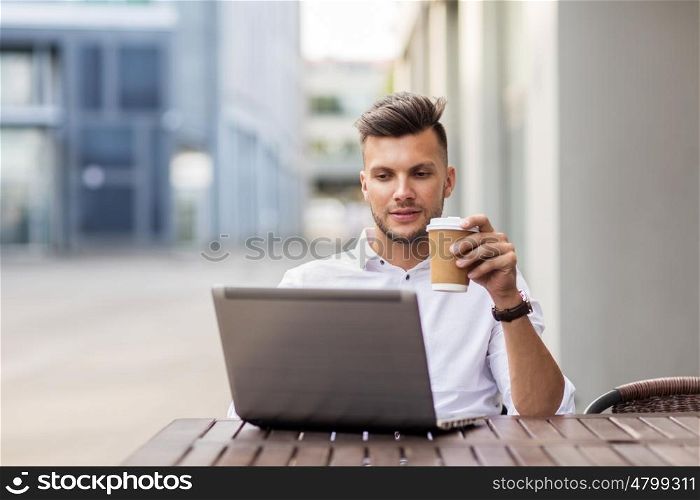 business, technology and people concept - young man with laptop computer and coffee cup at city street cafe