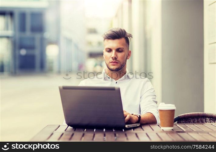 business, technology and people concept - young man with laptop computer and coffee cup at city street cafe. man with laptop and coffee at city cafe