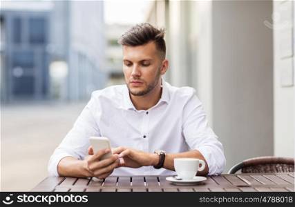 business, technology and people concept - young man with smartphone and coffee cup texting at city street cafe