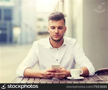business, technology and people concept - young man with smartphone and coffee cup texting at city street cafe. man with smartphone and coffee at city cafe