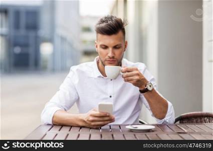 business, technology and people concept - young man with smartphone drinking coffee and texting at city street cafe