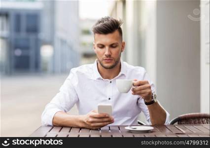 business, technology and people concept - young man with smartphone drinking coffee and texting at city street cafe