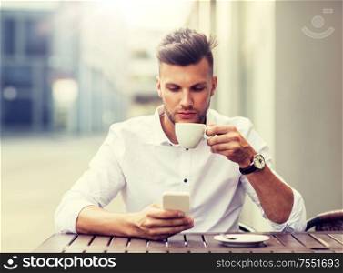 business, technology and people concept - young man with smartphone drinking coffee and texting at city street cafe. man with smartphone drinking coffee at city cafe