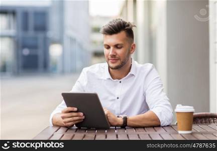 business, technology and people concept - young man with tablet pc computer and coffee cup at city street cafe