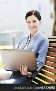 business, technology and people concept - young smiling woman with laptop computer sitting on bench in city