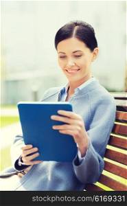 business, technology and people concept - young smiling woman with tablet pc computer sitting on bench in city
