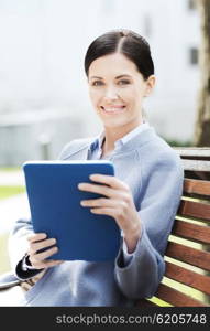 business, technology and people concept - young smiling woman with tablet pc computer sitting on bench in city