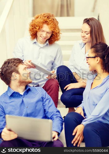 business, technology and startup concept - smiling creative team with laptop and tablet pc computer sitting on staircase