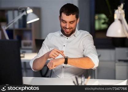 business, technology and time management concept - happy smiling businessman with smart watch at nigh office. happy businessman with smart watch at nigh office