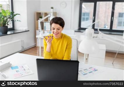 business, technology and ui design concept - smiling creative woman with laptop computer and user interface templates using voice command recorder on smartphone at office. designer recording voice by smartphone at office