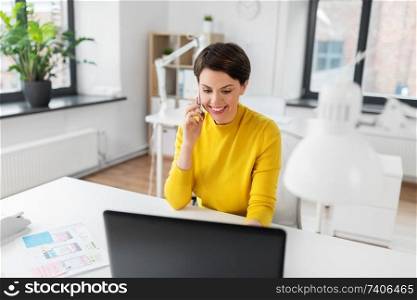 business, technology and ui design concept - smiling creative woman with laptop computer and user interface templates calling on smartphone at office. happy ui designer calling on smartphone at office