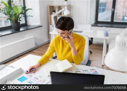 business, technology and ui design concept - smiling creative woman with user interface templates calling on smartphone and writing to notebook at office. happy ui designer calling on smartphone at office