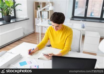 business, technology and user interface design concept - smiling ui designer with user interface templates and notebook using smartphone at office. smiling ui designer using smartphone at office