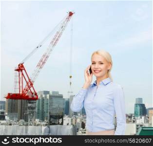 business, technology, building and people concept - smiling young businesswoman with smartphone over city building background
