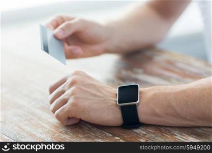 business, technology, cash free and internet people concept - close up of male hands with smart watch and credit card at office